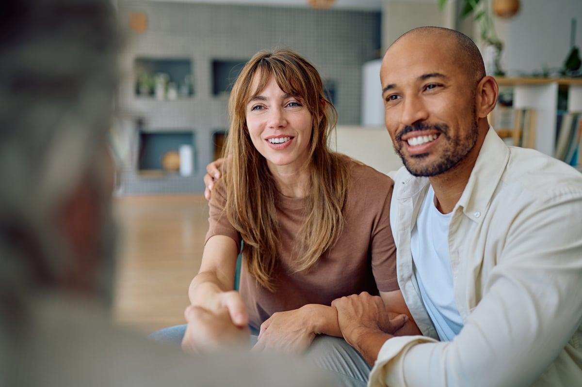 Young couple smiling and shaking hands with a financial consultant during a meeting at home, discussing investment and future planning